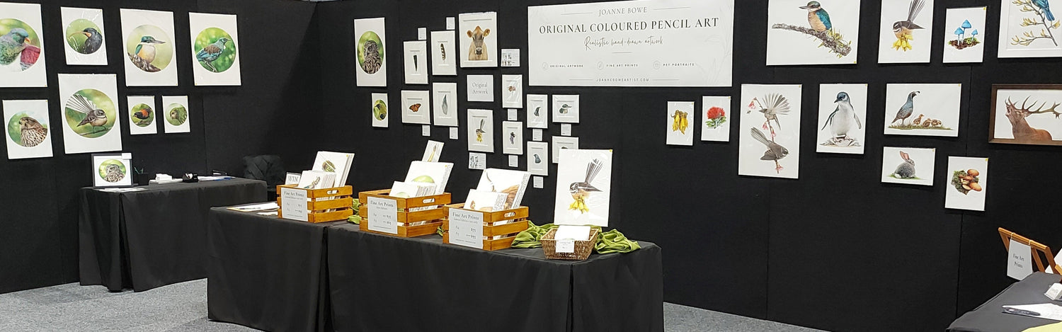 An indoor exhibition booth displaying coloured pencil artwork by joanne bowe new zealand artist.