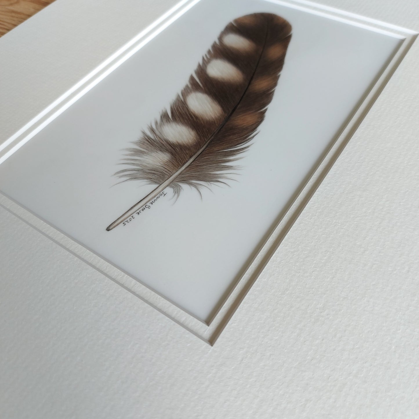 Angled view of the original ruru feather artwork, showing surface texture and tonal depth.